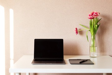 Laptop, bouquet of tulips and graphics tablet on white table. Work space.