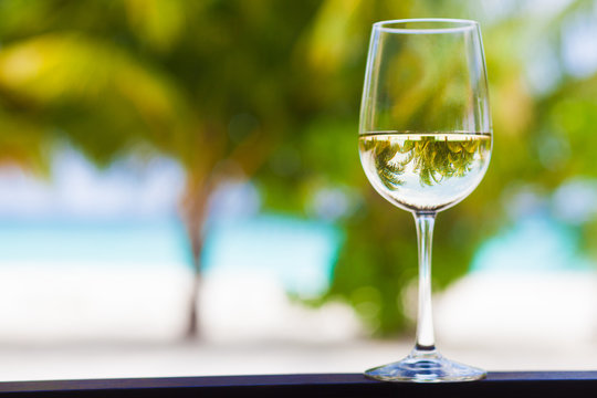 glass of chilled white wine and sunglasses on table on a tropical background