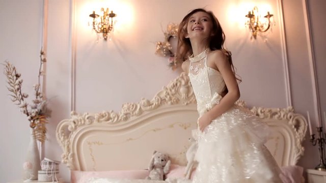 Little girl in a snow-white dress jumps on a luxurious bed