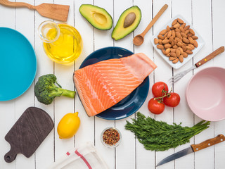 Piece of fresh salmon on a plate, avocado, almonds, sunflower oil and vegetables on a table