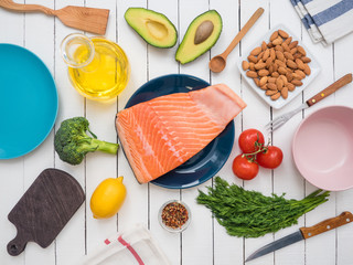 Piece of fresh salmon on a plate, avocado, almonds, sunflower oil and vegetables on a table