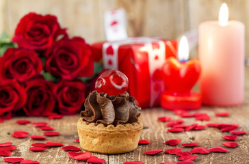 Cupcake with cherry in front of bouquet of red roses