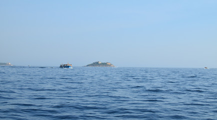 Obraz premium Tourist boat sailing on a sea passing an island on its way