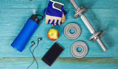 Weight plates, gloves and smartphone on wooden background