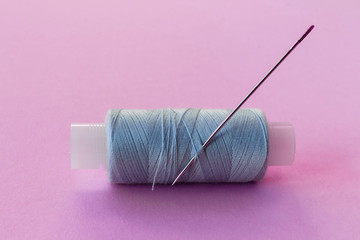 Multicolored threads, scissors, buttons, fabric and various sewing accessories on a pink background with copy space flat lay
