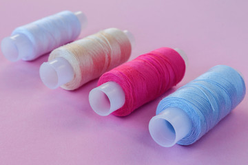 Multicolored threads, scissors, buttons, fabric and various sewing accessories on a pink background with copy space flat lay