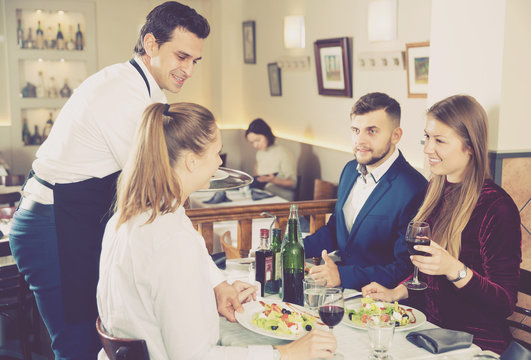 Handsome waiter serving meals to friendly company visitors