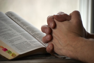 Naklejka premium Man holding his hands close to the bible and praying.