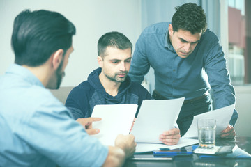 Three upset males with papers at table