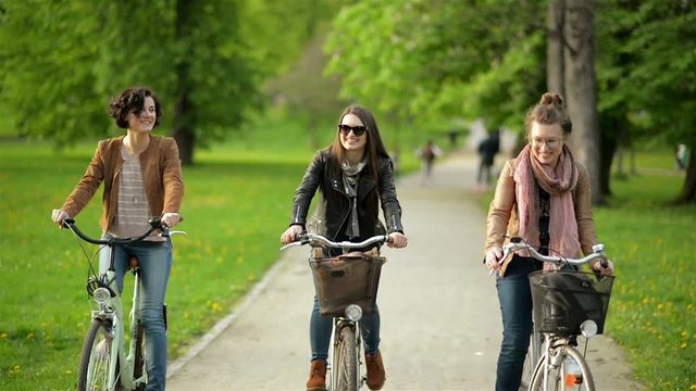 Funny Urban Biking in the Park of Three Cute Female Friends with Amazing Smiles. First Woman has Short Curly Hair, the Second Wearing Sunglasses and the Third has Eyeglasses.