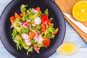 Fresh and tasty spring salad in a black plate on a rustic wooden background
