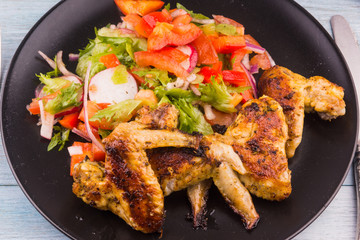 Delicious fried chicken wings on a plate with vegetable salad close-up