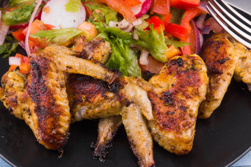 Delicious fried chicken wings on a plate with vegetable salad close-up