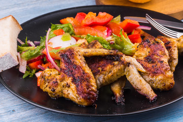 Delicious fried chicken wings on a plate with vegetable salad close-up