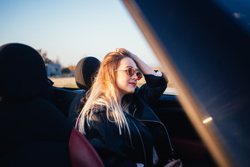 Attractive, beautiful and sexy young blonde woman sits inside convertible cabriolet car, fixes hair...