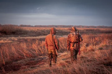 Papier Peint photo Lavable Chasser Hunters hunting in rural field during sunrise. Field painted with orange color of rising sun