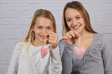 Portrait of two cute smiling sisteteenage girls holding handmade heart shape decorations. Love,...