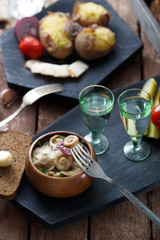 Pickled tomatoes, cucumbers, mushrooms and onion on wooden background with fork and shots of vodka.