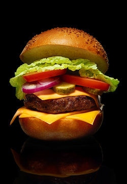 Hamburger with cheese, pickles, tomato, onions, lettuce on black