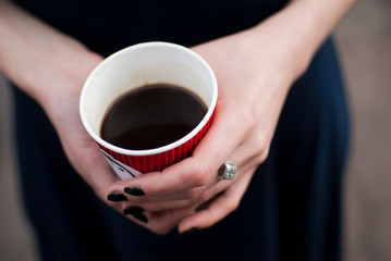 Girl holding red paper cup of black cofee in her hands 