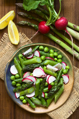 Fresh green asparagus, radish and pea salad served on plate, ingredients on the side, photographed overhead with natural light