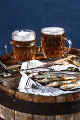 Beer mugs with dried fishes on a wooden barrel