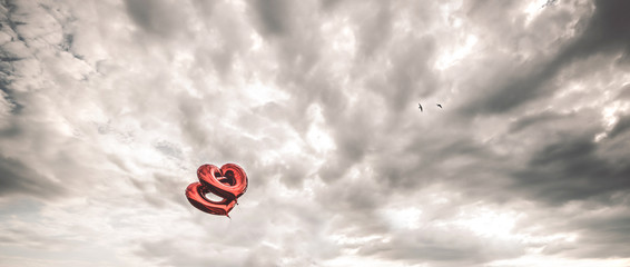 Two red heart-shaped balloons in the air. Beautiful background with stormy sky.