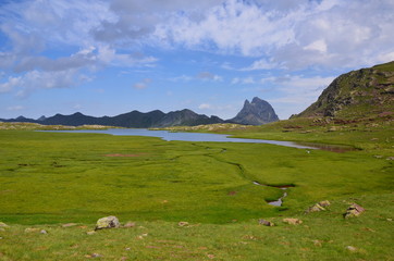 Fototapeta na wymiar Green meadow with blue lake and mountain range in the background