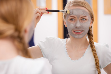 Happy young woman applying mud mask on face