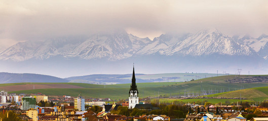 Town and peak of cathedral tower behind snow-caped mountains © NemanTraveler