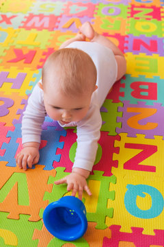 Cute baby in white vest, reaching for cups while on lying on tummy on alphabet mat.