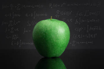 Green apple on black table against blackboard full of mathematical formulas