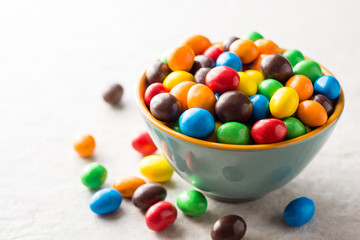 Colorful chocolate buttons in bowl on gray stone background.