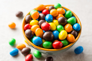 Colorful chocolate buttons in bowl on gray stone background.