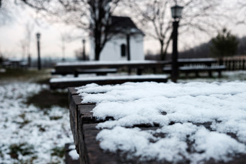 wooden desk in garden covered by snow, lamps and small church in background