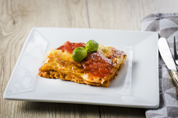 appetizing portion of lasagna on a white plate with tomato sauce