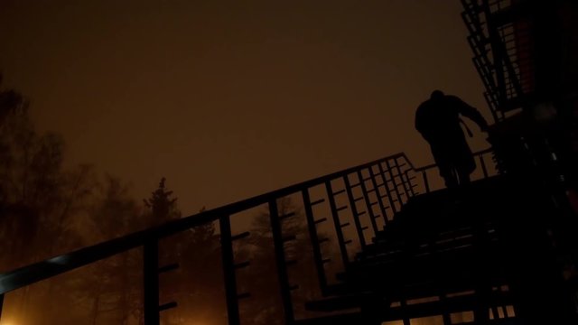 4k Black silhouette climbs the stairs in dark noir city