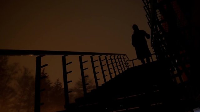 4k Black silhouette descends the stairs at the dark cold city with red sky