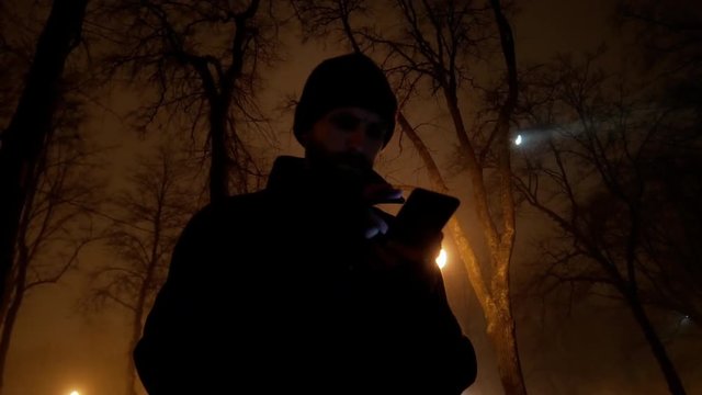 4k Middle age danger man with mobile phone in winter night cold city park lowlight