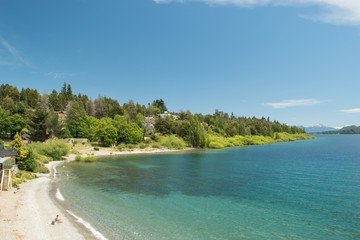 Fototapeta na wymiar Costa frente a lago turquesa con bosque de fondo y cielo azul