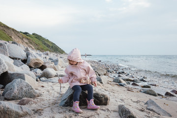 little girl playing on the beach wearing a raincoat and wellies