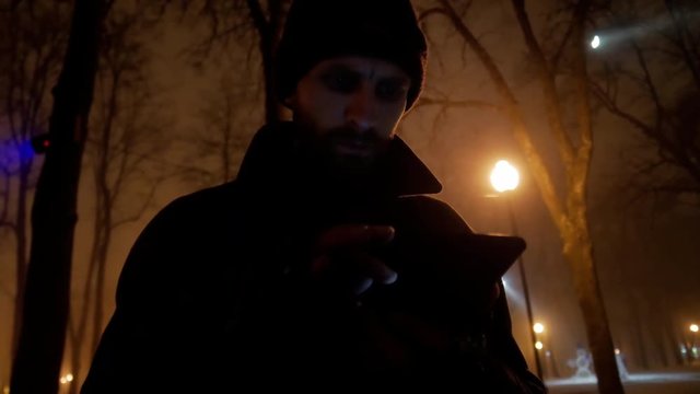 4k Bearded danger middle age man reads messages in cold dark winter city park close-up  
