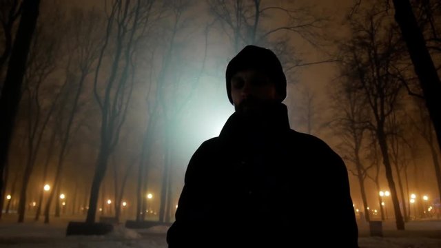 4k Black silhouette of man walks at dark winter night park with backlight close-up