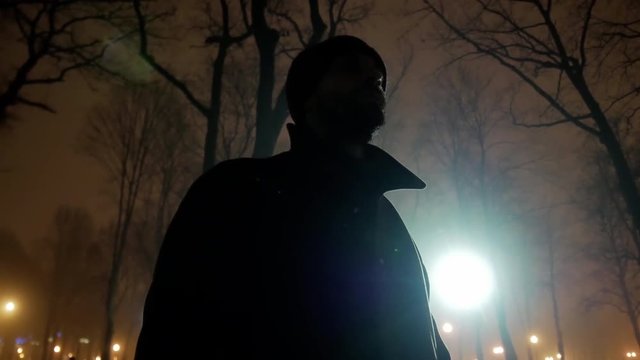 4k Silhouette of middle age bearded  brutal man with baclkight in night dark park lowlight