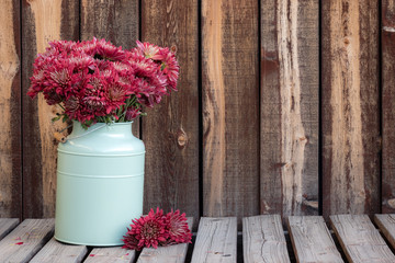 Large bouquet of mums in a green container on a rustic wooden table with a stem of mums on the side.