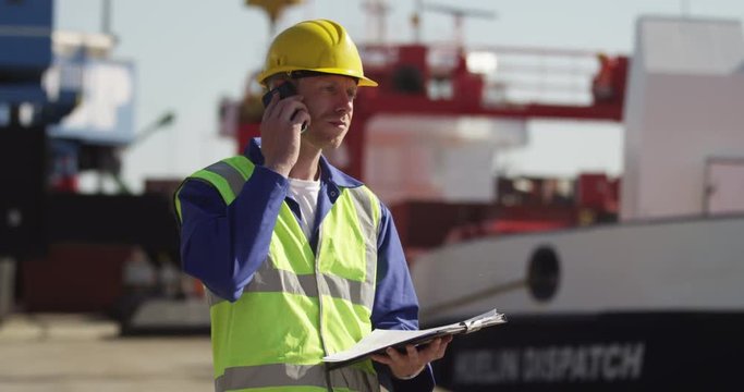 A dock worker standing at the harbor amidst shipping industry activity. Shot on RED Epic.