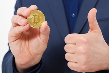 Handsome confident businessman holding gold bitcoin coin. Selective focus. Business success concept. Big thumb up.