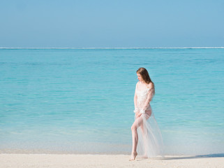 Fototapeta na wymiar Young beautiful woman in dress on the seashore Maldives. Beautiful and fashion woman with long legs in white dress, posing on the tropical beach. Girl on a beach in white dress rest near blue lagoon.