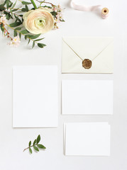 Feminine wedding, birthday desktop mock-ups. Blank greeting cards, envelope. Eucalyptus branches, pink cherry tree blossoms and Persian buttercup flowers. White table background. Flat lay, top view.