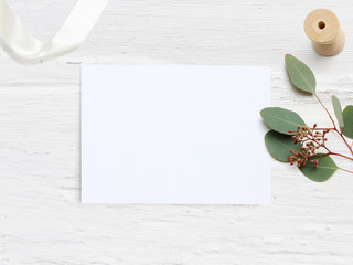 Feminine wedding desktop mock-up with blank paper card and Eucalyptus populus branch on white shabby table background. Empty space. Styled stock photo, web banner. Flat lay, top view.